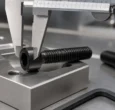 Black oxide socket head cap screw measured with a precision caliper in a machined aluminum fixture