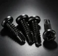 Black cross-recessed self-drilling screws on a dark industrial surface